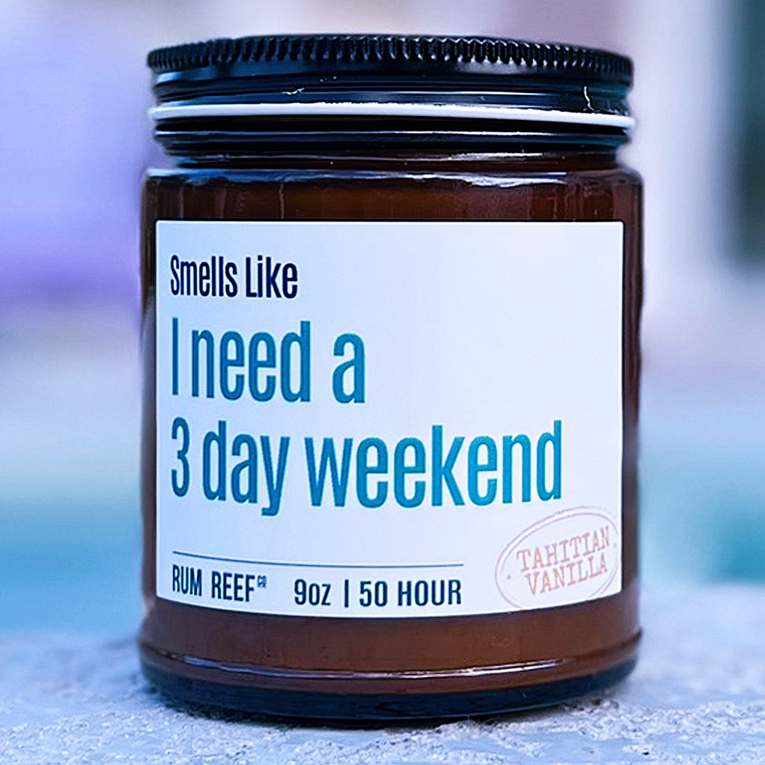 Candle jar with a label reading 'Smells Like I need a 3 day weekend' on a blurred background